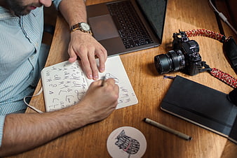 Man sketching design notes on desk with camera and laptop
