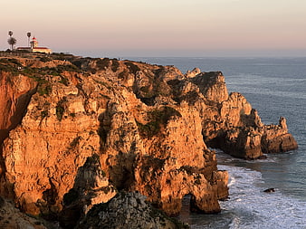 Lighthouse on Rocky Cliffs at Sunset Over the Ocean