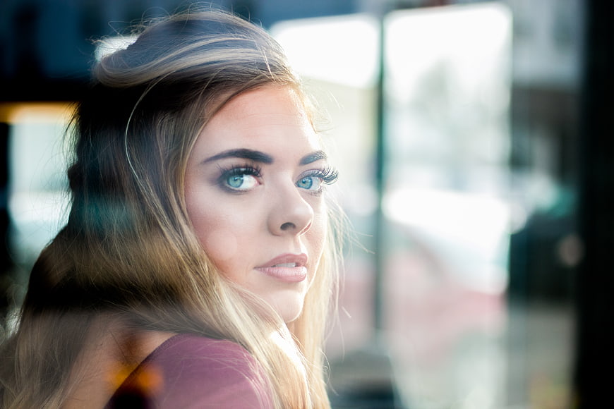 Close-up portrait of blonde woman looking through glass window