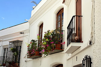 White Spanish building with flower-filled balconies and blue sky