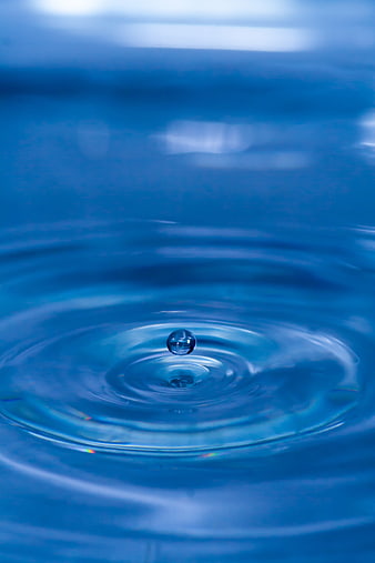 Macro shot of a water droplet bouncing on a blue rippling water surface