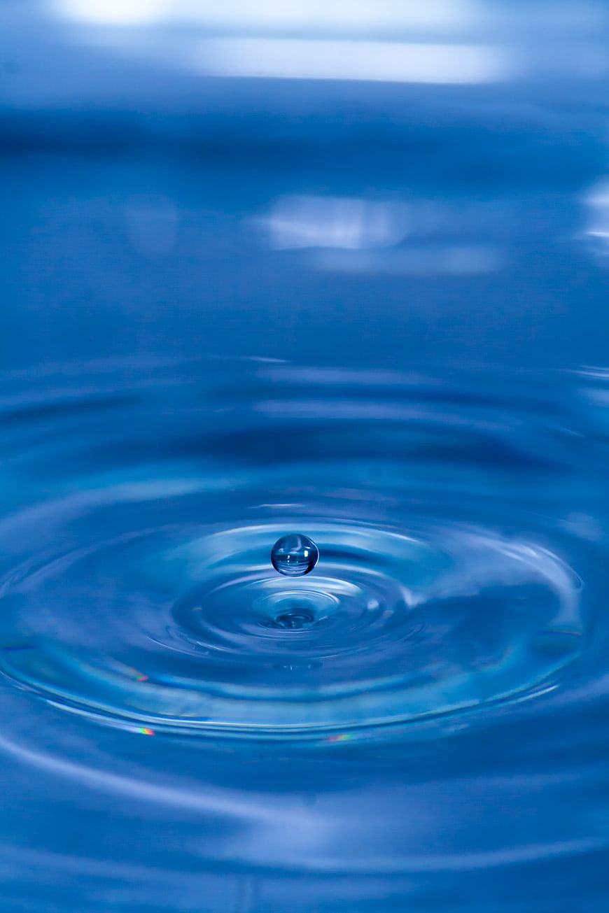 Macro shot of a water droplet bouncing on a blue rippling water surface