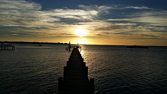 Silhouette of wooden pier at sunset over calm water