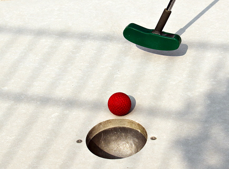 Red mini golf ball and green putter near hole