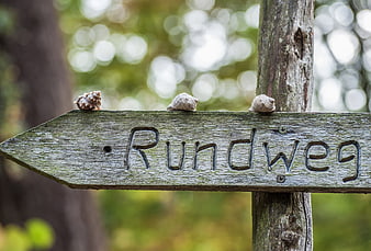 Weathered wooden sign reading Rundweg with three snails on top