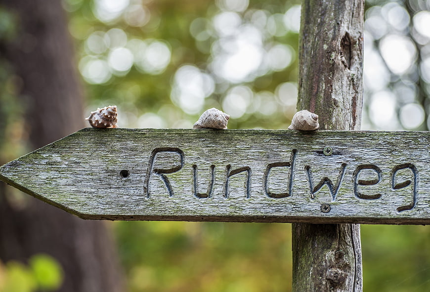 Weathered wooden sign reading Rundweg with three snails on top