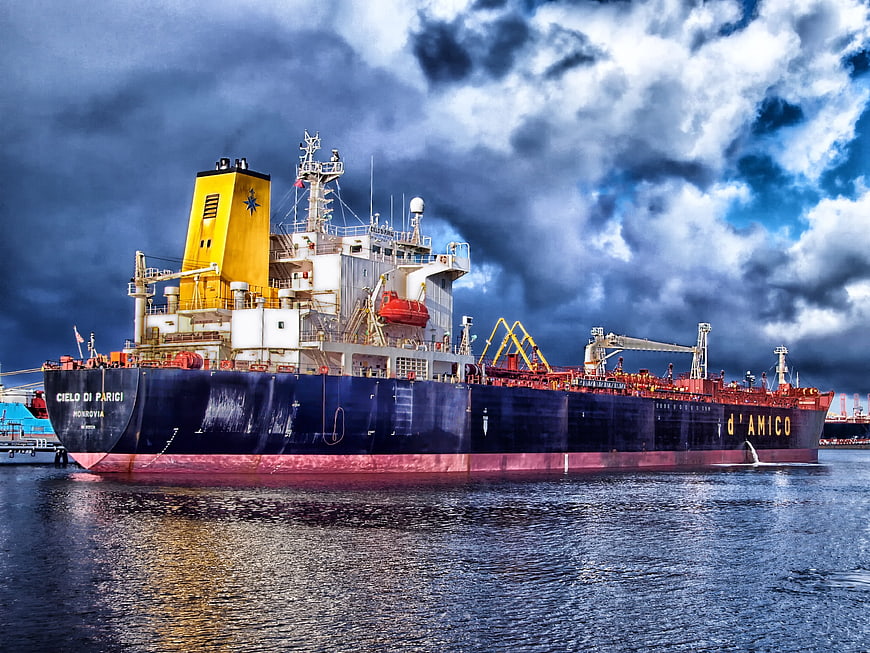 Large cargo ship docked in harbor under dramatic cloudy sky