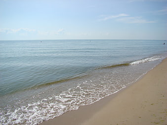 Calm ocean waves washing onto sandy beach under blue sky