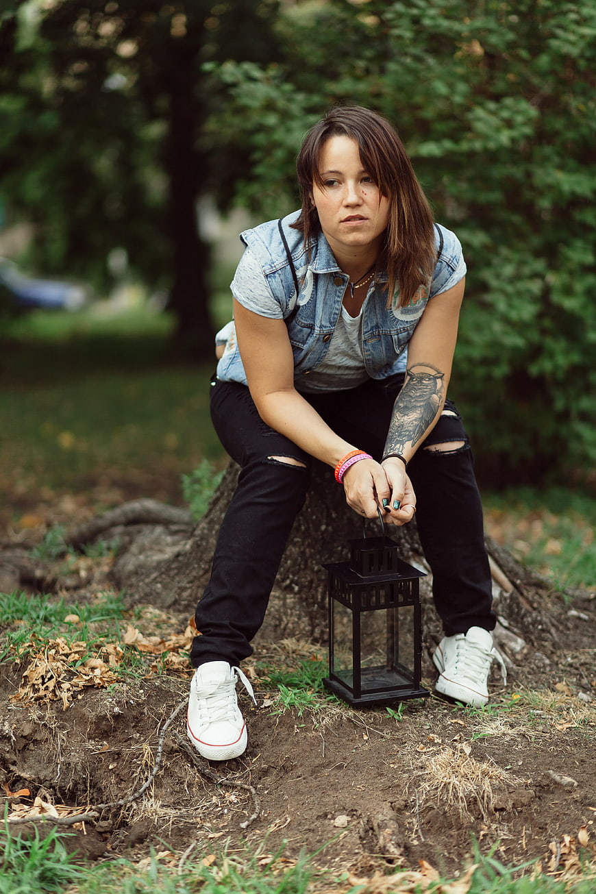Woman with Denim Vest and Lantern Sitting on Tree Roots