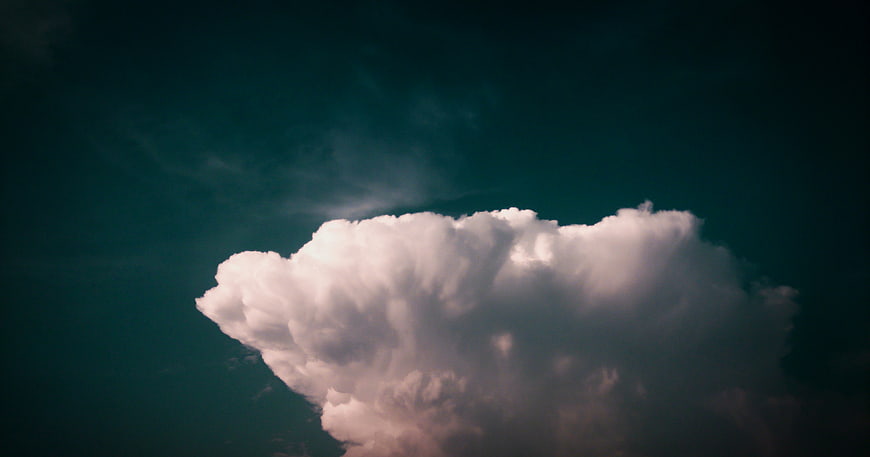 Dramatic white cumulus cloud against dark teal sky background