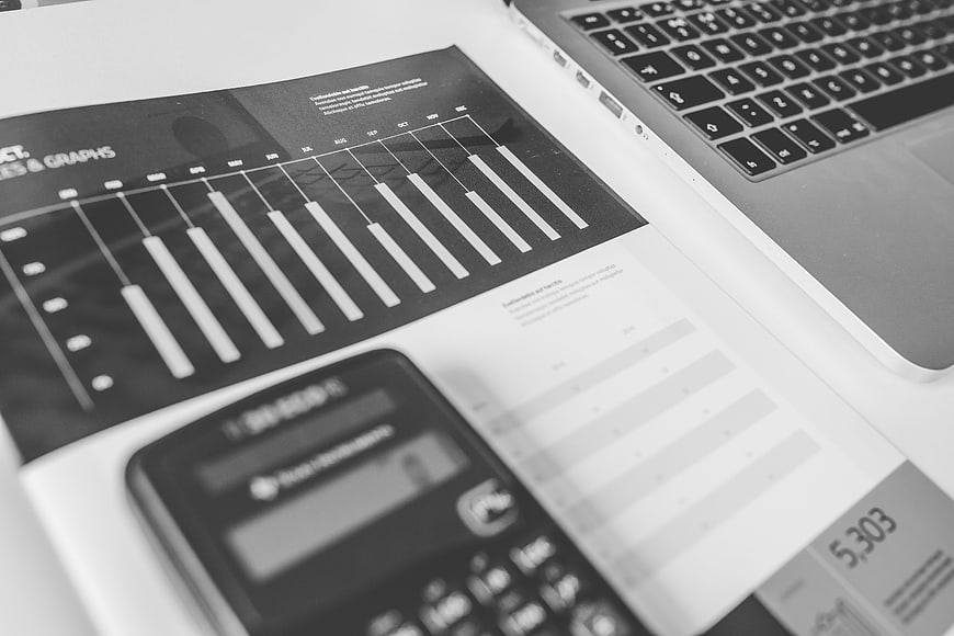 Black and white calculator, laptop, and financial charts on desk