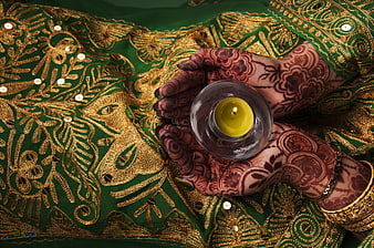 Henna-decorated hands holding a candle on green embroidered fabric