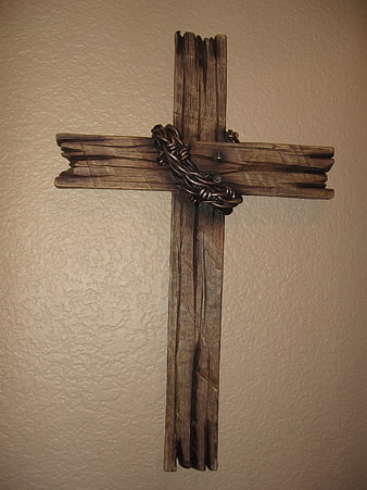 Rustic wooden cross with metal crown of thorns on textured beige wall