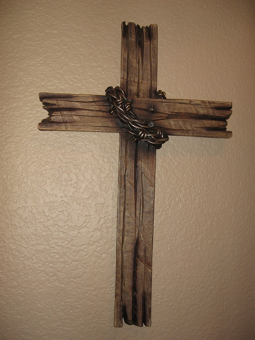 Rustic wooden cross with metal crown of thorns on textured beige wall