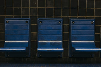Three worn blue metal subway seats against dark tiled wall