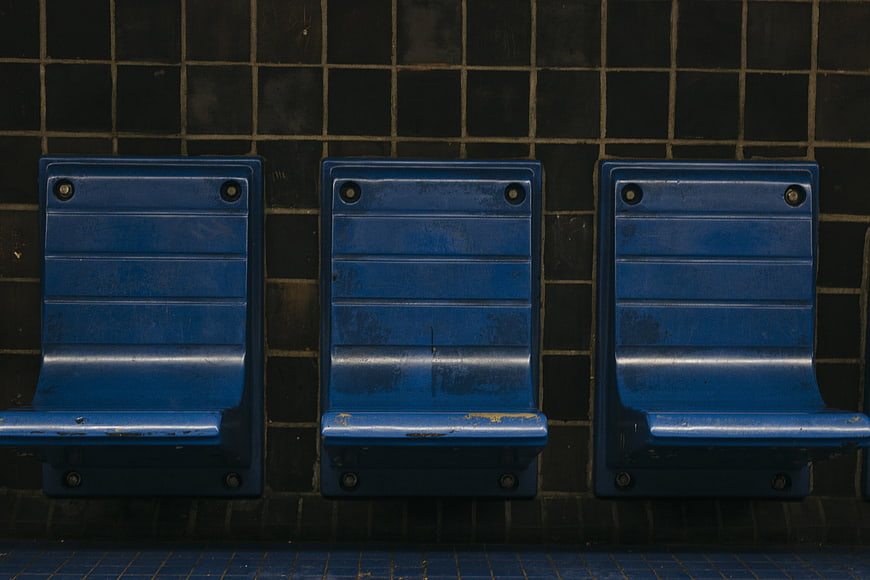 Three worn blue metal subway seats against dark tiled wall