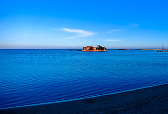 Serene Blue Sea with Distant Island Building and Sandy Shore