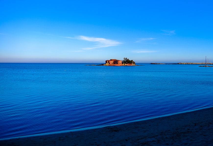 Serene Blue Sea with Distant Island Building and Sandy Shore