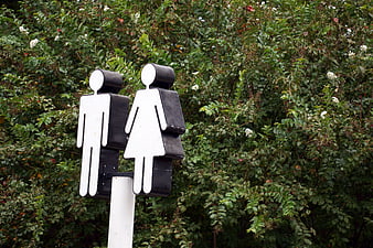Black and white restroom sign with male and female figures against green foliage
