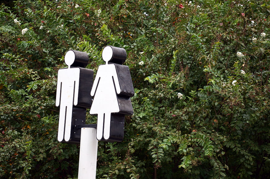 Black and white restroom sign with male and female figures against green foliage