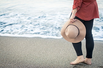 Woman holding hat on sandy beach with ocean waves