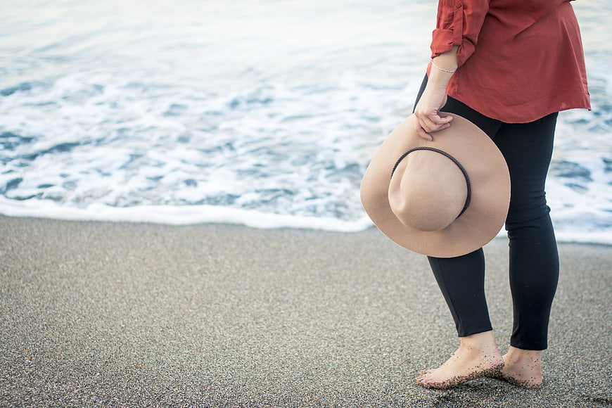 Woman holding hat on sandy beach with ocean waves