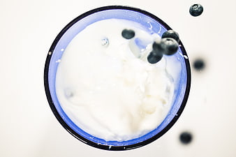 Top View of Blueberries Falling into Yogurt in Blue Bowl