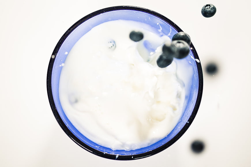 Top View of Blueberries Falling into Yogurt in Blue Bowl