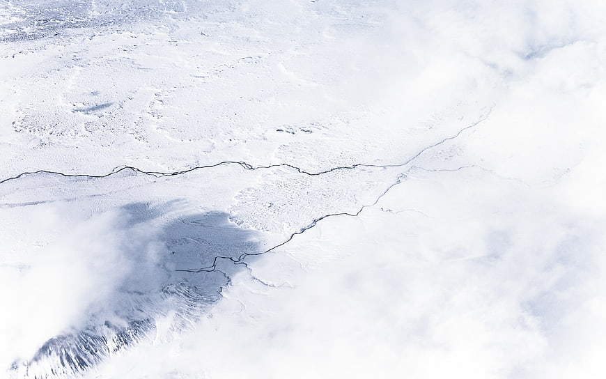 Aerial view of snow-covered landscape with winding river and clouds
