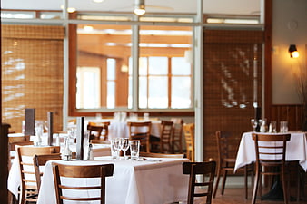 Empty restaurant dining room with white tablecloths and wooden chairs