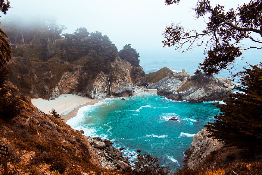 Misty coastal waterfall cascading into turquoise ocean cove