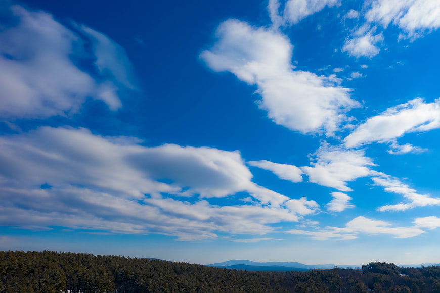 Blue Sky with White Clouds Over Forested Mountain Landscape