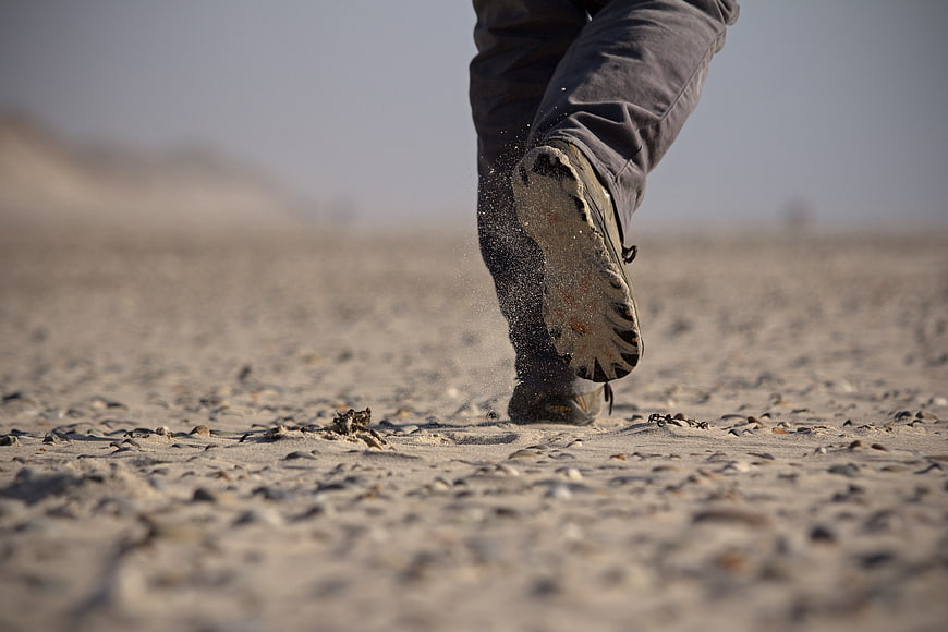 Close-up of hiking boots walking on sandy beach
