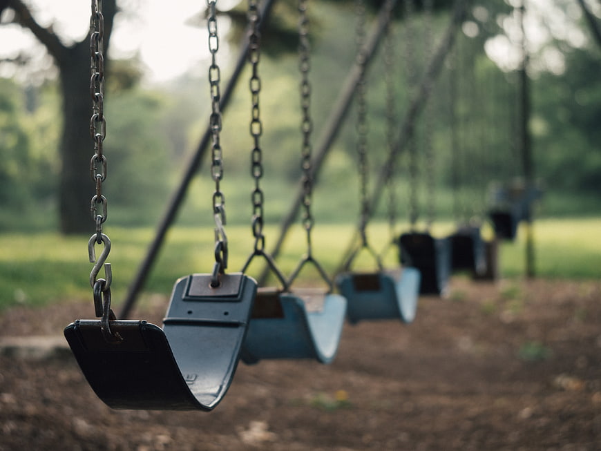 Empty playground swings in a park with blurred green background