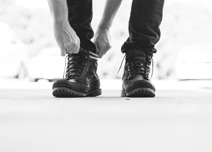 Man tying black leather boots in black and white