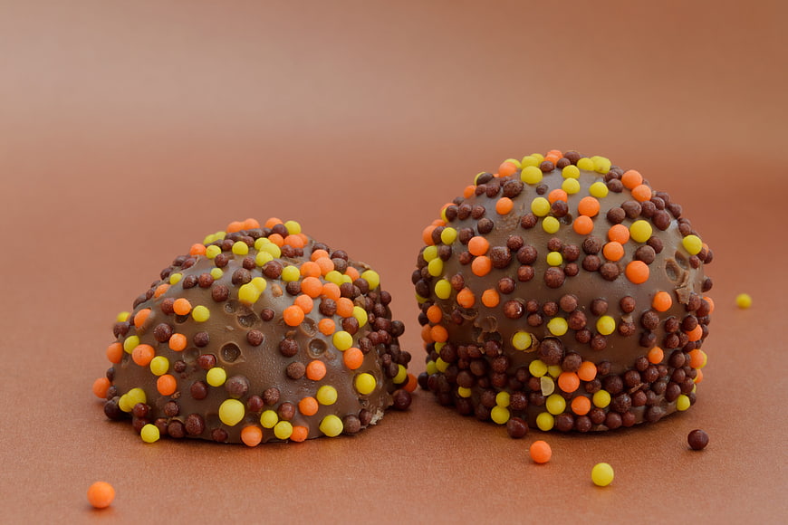 Two Chocolate Easter Eggs With Colorful Sprinkles On Brown Background