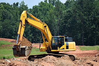 Yellow Excavator Digging Red Clay Soil In Forested Construction Site