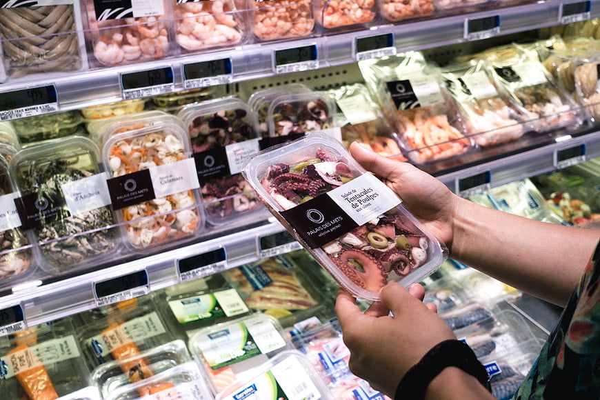 Hands holding packaged octopus salad in grocery store seafood section