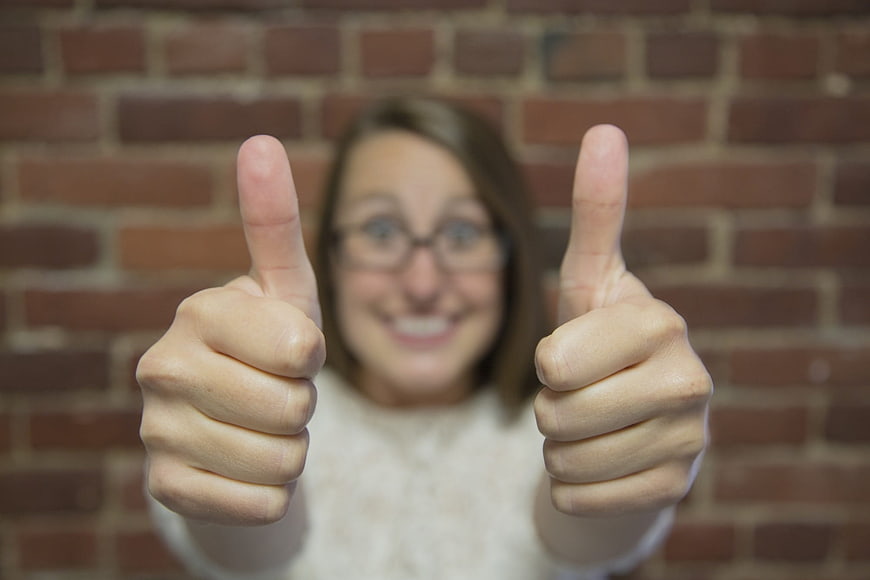 Woman Giving Double Thumbs Up Gesture Against Brick Wall