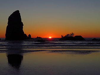 Silhouette of sea stack at sunset on wet beach