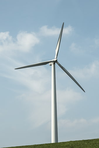White Wind Turbine on Green Hill Against Blue Sky