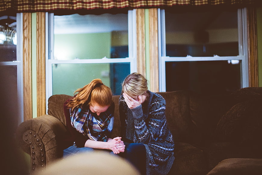 Two Sad Women Sitting on Couch Comforting Each Other
