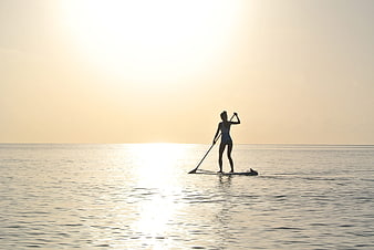 Silhouette of woman paddleboarding on calm ocean at sunrise