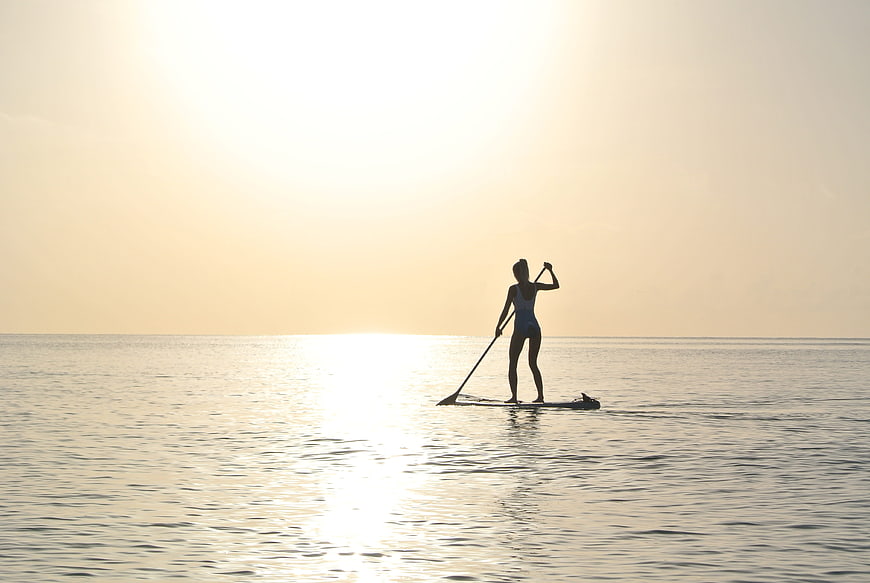 Silhouette of woman paddleboarding on calm ocean at sunrise