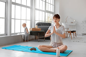 Mother meditating at home with toddler playing nearby