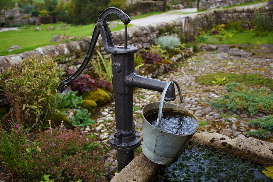 Vintage black hand pump with metal bucket in garden
