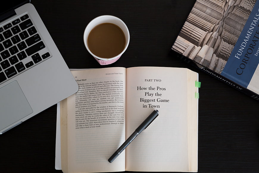 Open finance book with laptop and coffee on dark desk