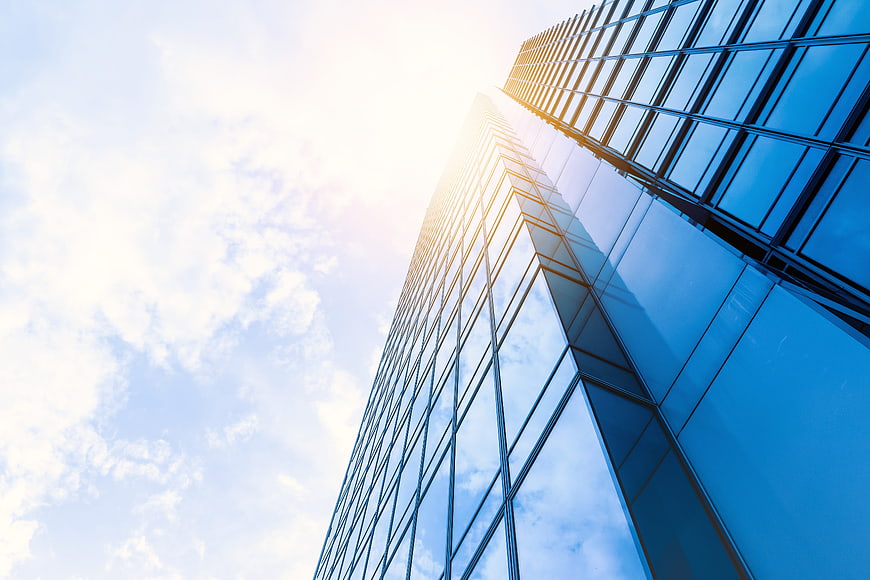 Low angle view of modern glass skyscraper against blue sky