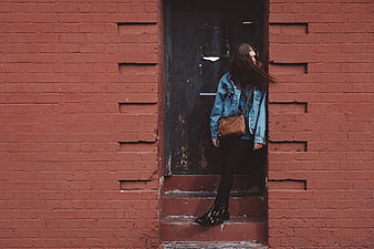 Woman in denim jacket standing by red brick wall