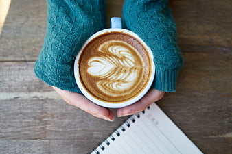 Hands holding latte art coffee cup on wooden table
